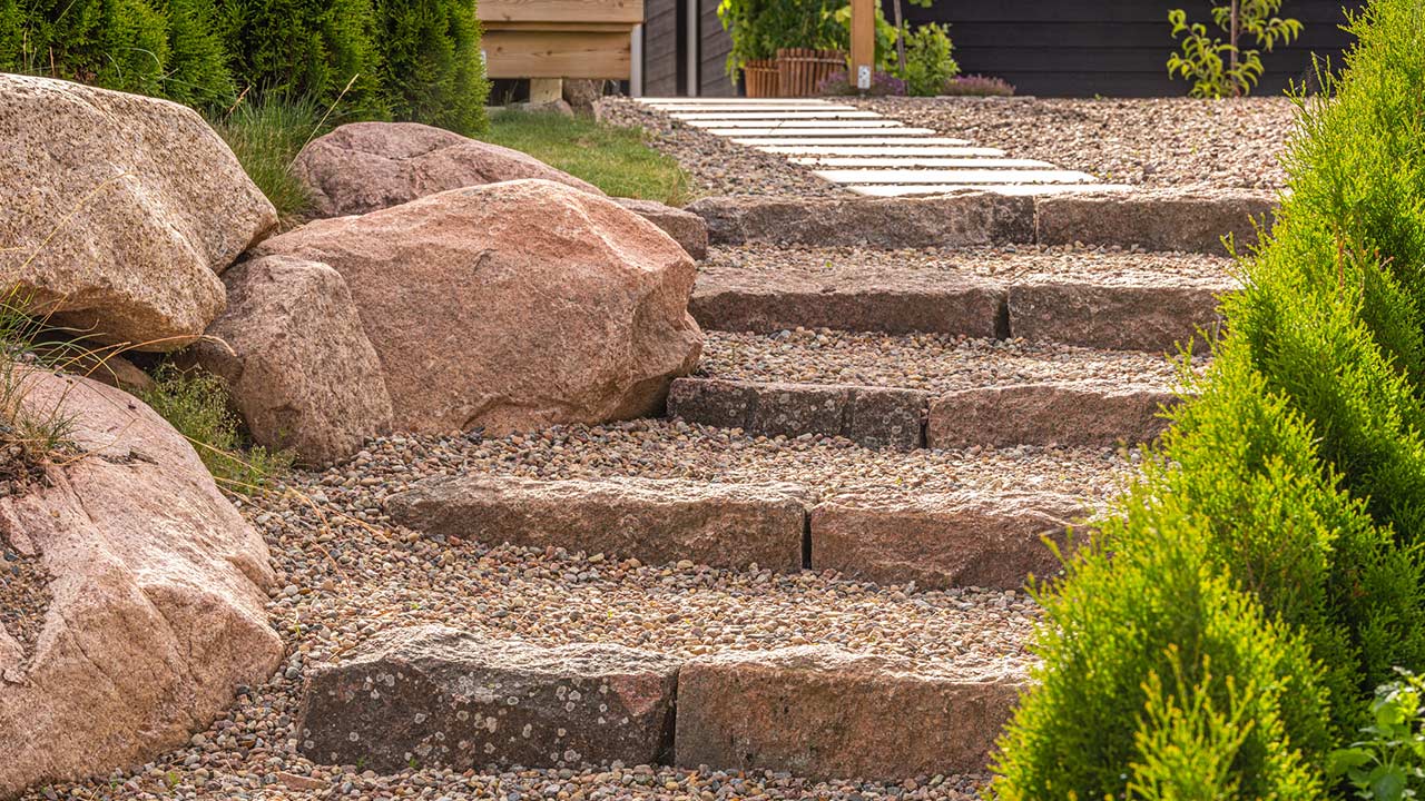 Mur av natursten i tomtgräns för den sluttande tomten till nybyggd villa. Därefter satte vi ytterligare murar, singelytor och trappor i natursten.